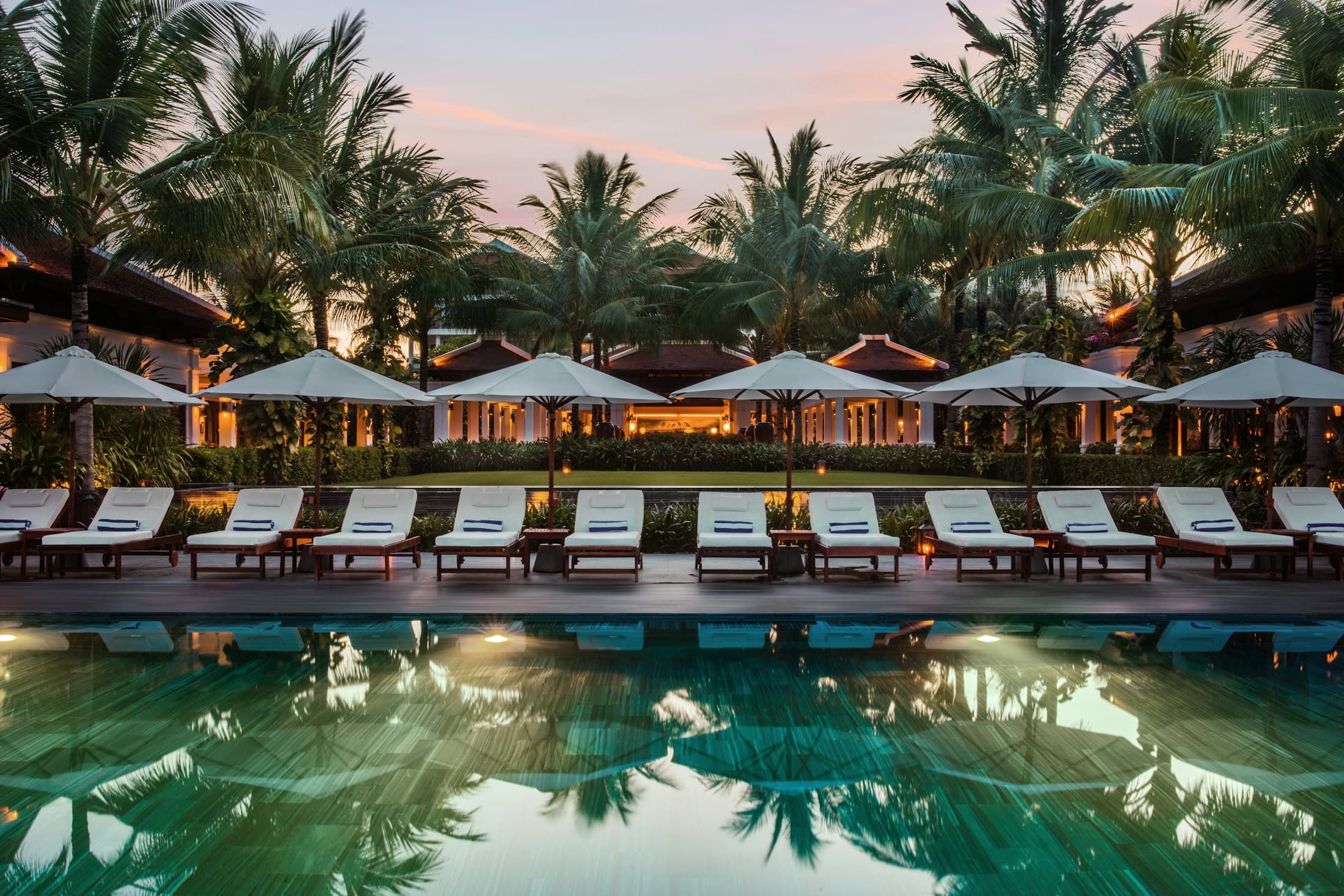 Piscine d'un resort au crépuscule, palmiers et transats